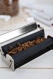 Photo of Roller with tobacco on white wooden table, closeup. Making hand rolled cigarettes
