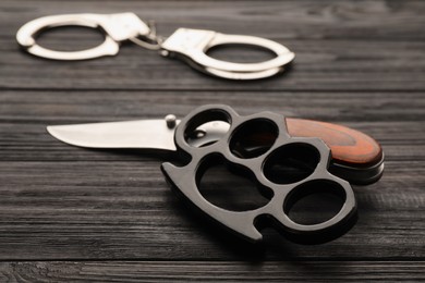 Brass knuckles, knife and handcuffs on black wooden background