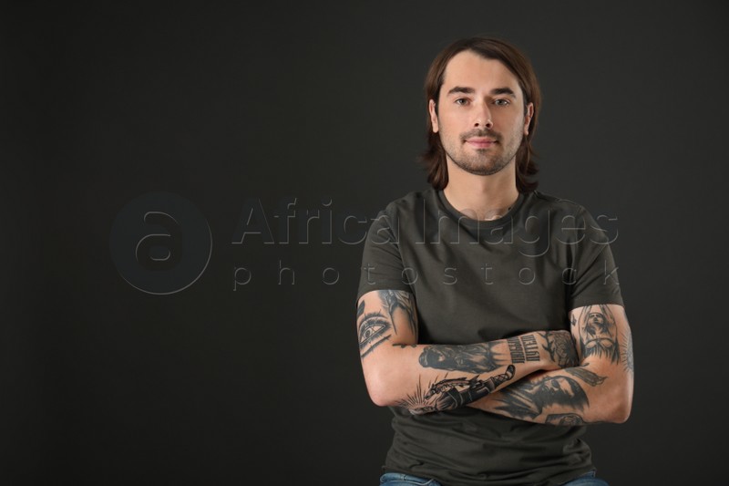 Young man with tattoos on arms against black background. Space for text