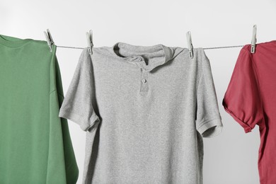 Different shirts drying on laundry line against light background, closeup