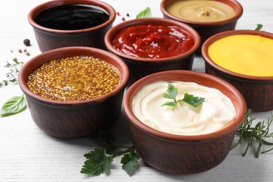 Many different sauces and herbs on white wooden table, closeup
