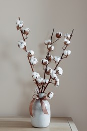 Vase with beautiful bouquet of white fluffy cotton flowers on wooden table in cozy room
