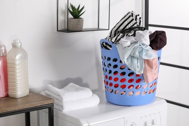 Photo of Laundry basket overfilled with clothes on washing machine in bathroom