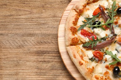 Photo of Tasty pizza with anchovies, arugula and olives on wooden table, top view. Space for text