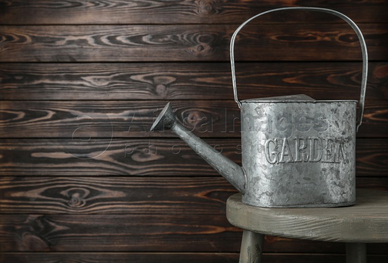 Photo of Vintage metal watering can on table against wooden background, space for text