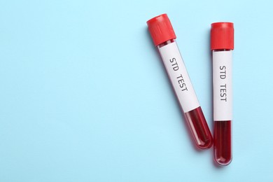 Tubes with blood samples and labels STD Test on light blue background, flat lay. Space for text