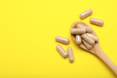 Many gelatin capsules and spoon on yellow background, flat lay. Space for text