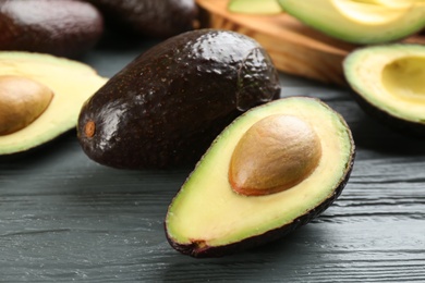 Whole and cut avocados on grey wooden table, closeup