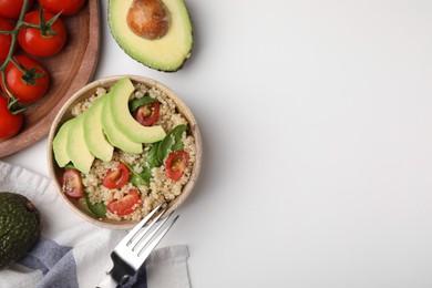 Photo of Delicious quinoa salad with tomatoes, avocado slices and spinach leaves served on white table, flat lay. Space for text