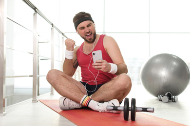 Lazy young man with sport equipment using smartphone on yoga mat
