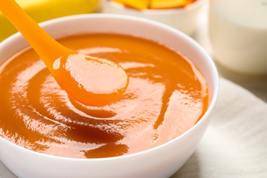 Spoon of healthy baby food over bowl, closeup