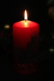 Red burning candle and fir tree branch in darkness, closeup view