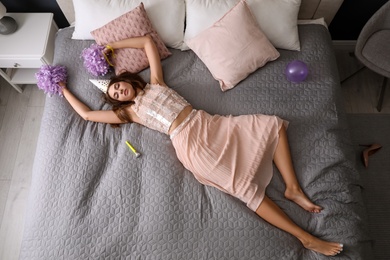 Exhausted woman in festive outfit sleeping on bed at home after party, above view