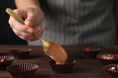 Professional confectioner making delicious chocolate candies at wooden table, closeup
