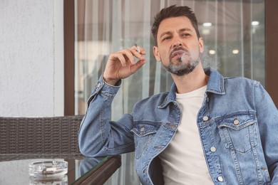 Photo of Handsome man smoking cigarette at table in outdoor cafe