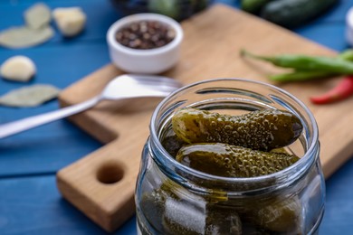 Photo of Jar of pickled cucumbers and ingredients for food preservation on blue wooden table, closeup