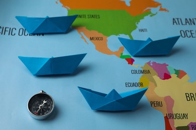 Bright paper boats and compass on world map, above view