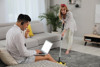 Man working on laptop while his wife cleaning carpet in living room. Stay at home concept