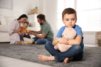 Unhappy little boy feeling jealous while parents spending time with his baby brother at home
