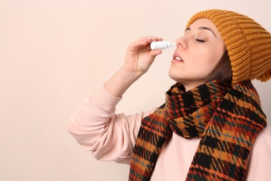 Woman using nasal spray on beige background, space for text