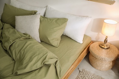 Comfortable bed with olive green linen in modern room interior