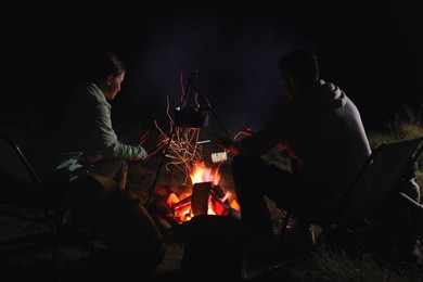 Couple warming hands near bonfire outdoors at night. Camping season