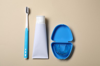 Photo of Toothpaste, brush and container with dental mouth guard on beige background, flat lay. Bite correction