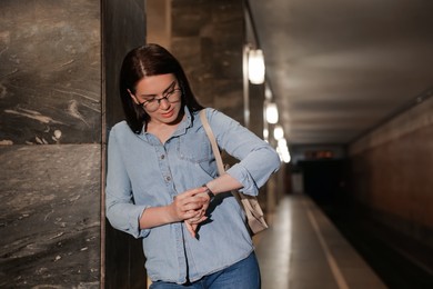 Photo of Beautiful woman with backpack looking at wristwatch on subway station. Public transport