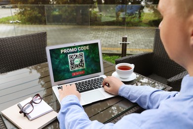 Man with laptop activating promo code at wooden table outdoors, closeup