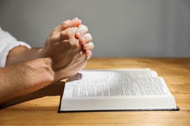Man with Bible praying at wooden table, closeup