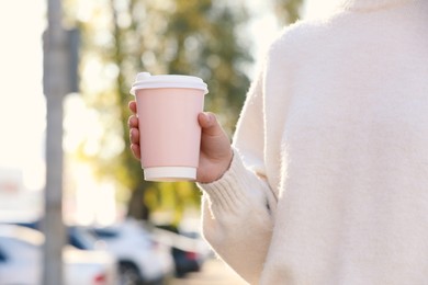 Photo of Woman holding pink takeaway cardboard cup on city street, closeup. Coffee to go