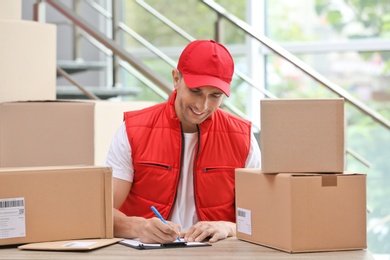 Young courier working with papers among parcels at table in delivery department