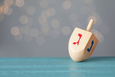 Hanukkah traditional dreidel with letters Gimel and Nun on wooden table against blurred lights. Space for text