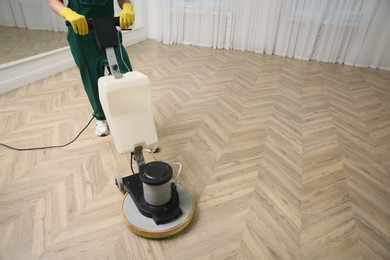 Professional janitor cleaning parquet floor with polishing machine indoors, closeup. Space for text