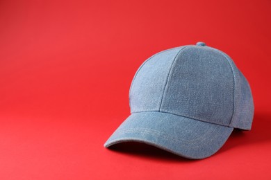 Stylish light blue denim baseball cap on red background. Space for text
