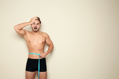 Fit man measuring his waist on color background, space for text. Weight loss
