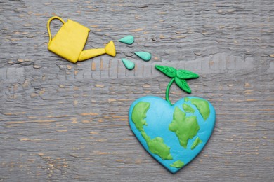 Happy Earth Day. Flat lay composition with plasticine planet and watering can on grey wooden table