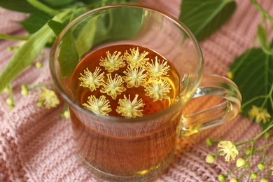 Glass cup of aromatic tea with linden blossoms on pink cloth, closeup