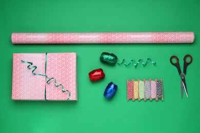 Flat lay composition with roll of wrapping paper, gift and accessories on green background
