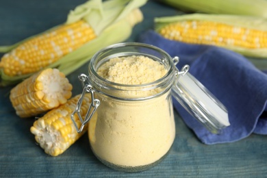 Corn flour in glass jar and fresh cobs on blue wooden table