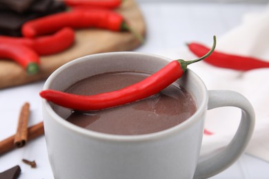 Photo of Cup of hot chocolate with chili pepper on white tiled table, closeup