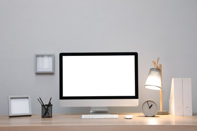 Comfortable workplace with blank computer display on desk near light grey wall. Space for text