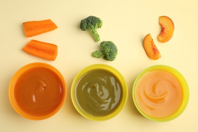Baby food in bowls and fresh ingredients on yellow background, flat lay