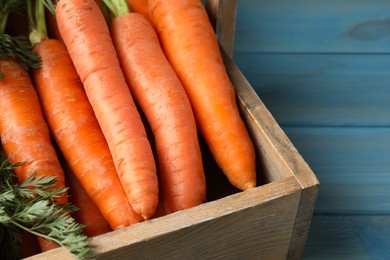 Fresh ripe juicy carrots in basket on light blue wooden table, closeup. Space for text