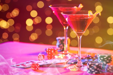 Cocktail, dice, playing cards and casino chips on table against blurred lights. Bokeh effect