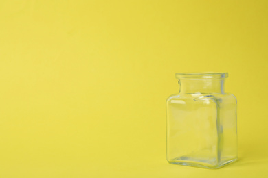 Open empty glass jar on light yellow background, space for text