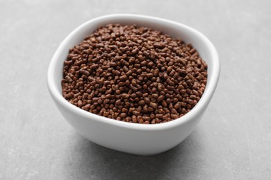 Photo of Buckwheat tea granules in bowl on light grey table, closeup