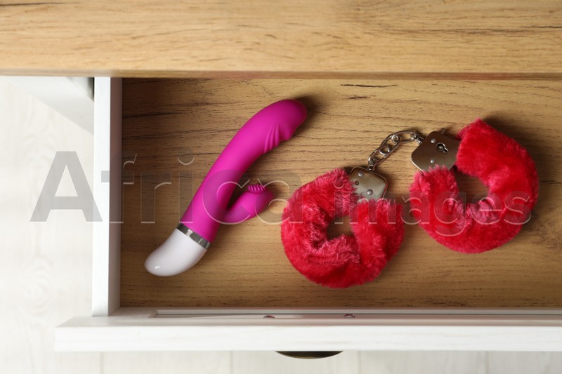 Fluffy handcuffs and vibrator in open wooden drawer, top view. Sex toys