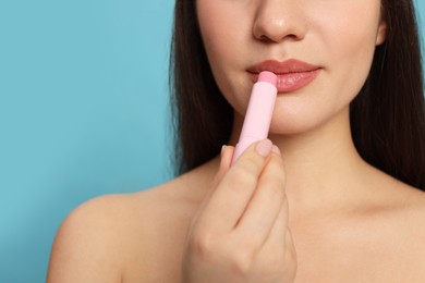 Young woman applying lip balm on turquoise background, closeup. Space for text