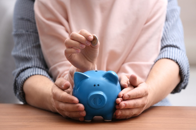 Couple with piggy bank and coin at wooden table, closeup